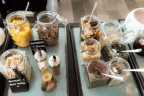 A display of various gluten-free and C-flakes products in glass jars with spoons.