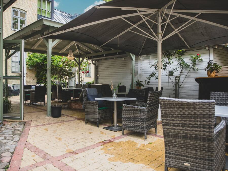 Un espacio al aire libre con patio, mobiliario de mimbre, un área de estar techada y plantas en macetas.