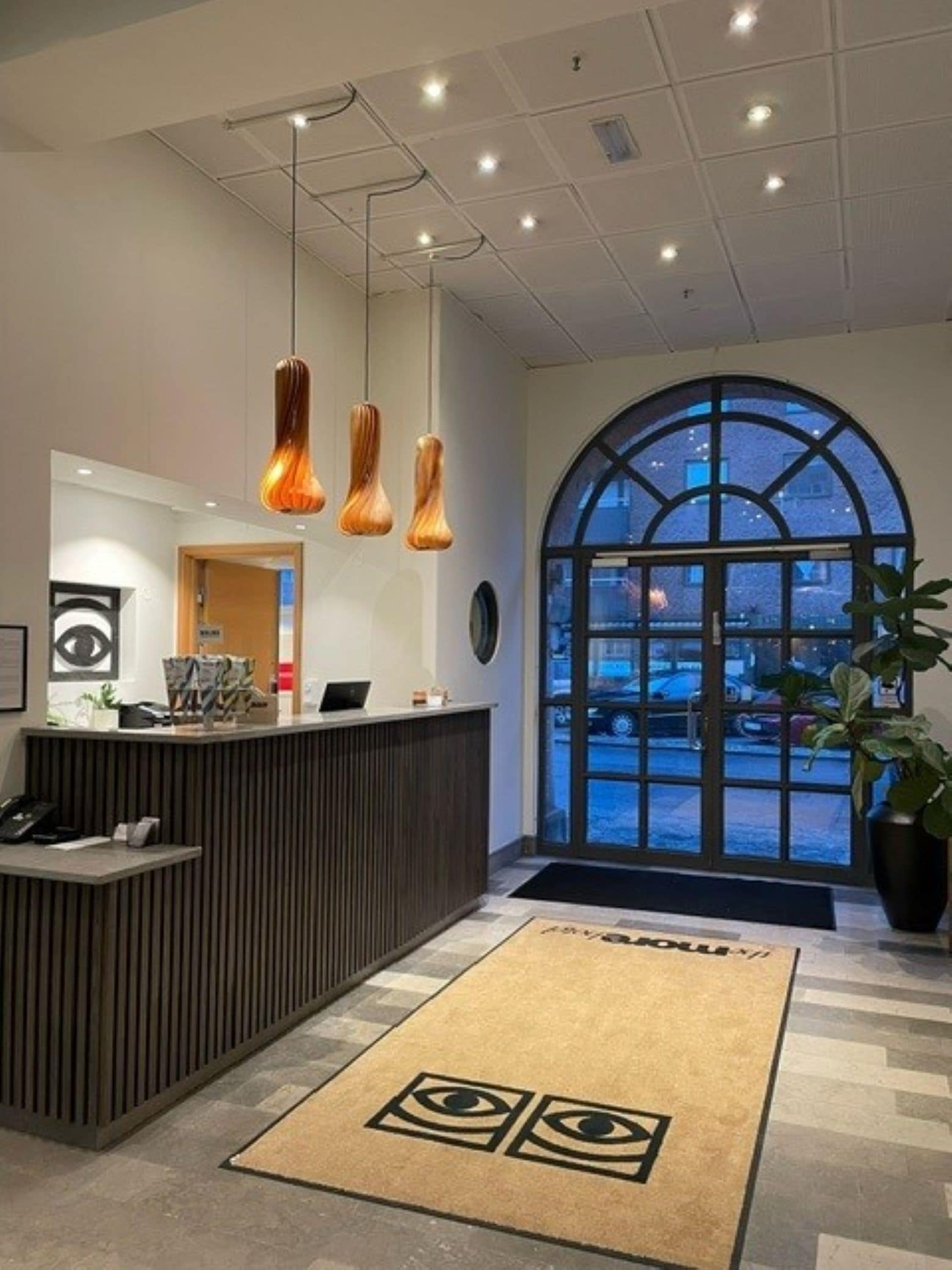 Uma área de recepção com design moderno, com balcão de atendimento, iluminação pendente e uma grande janela em arco que oferece vista para o exterior.