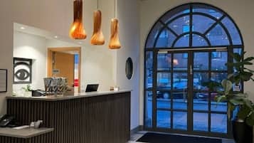Uma área de recepção com design moderno, com balcão de atendimento, iluminação pendente e uma grande janela em arco que oferece vista para o exterior.