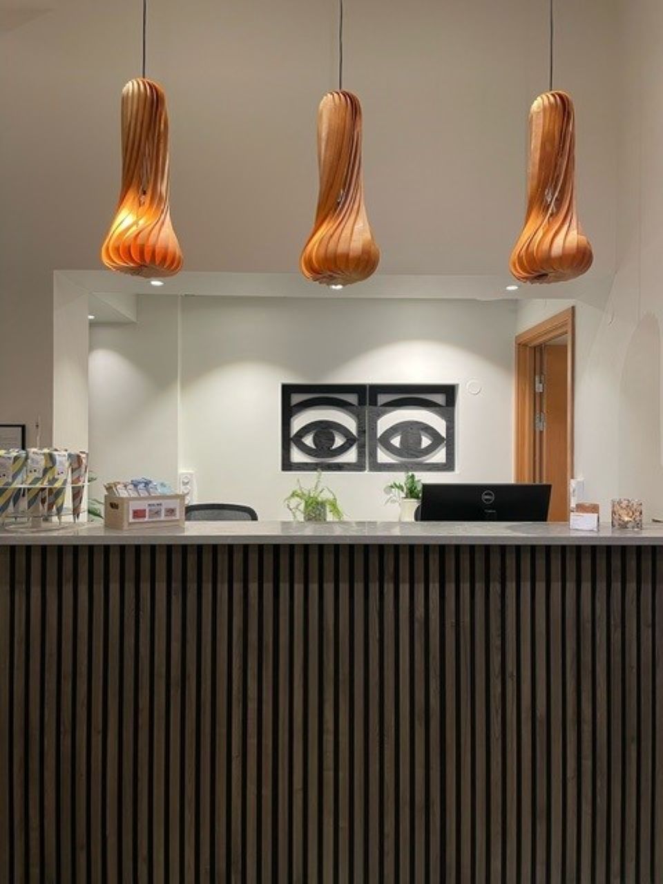 Un mostrador de recepción de diseño moderno, con frente de listones de madera y tres lámparas colgantes.