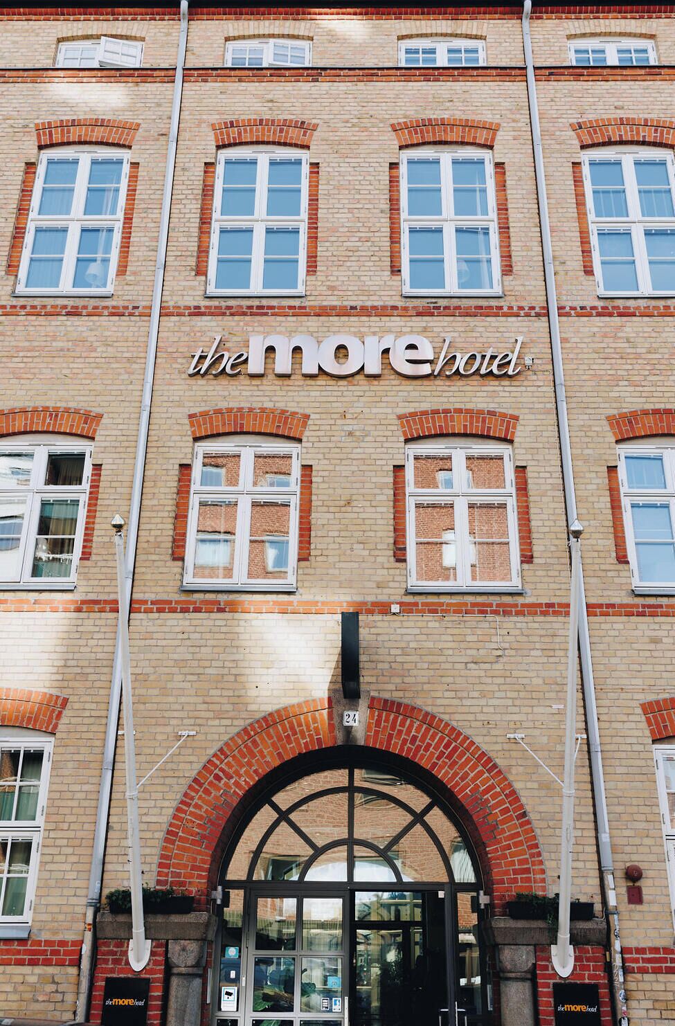 A hotel facade with a red brick exterior, multiple windows, and a prominent entrance with a glass door.