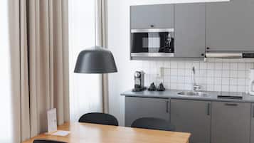 A modern kitchen with grey cabinets, a wooden dining table, two black chairs, a black pendant lamp, and a white tiled backsplash.