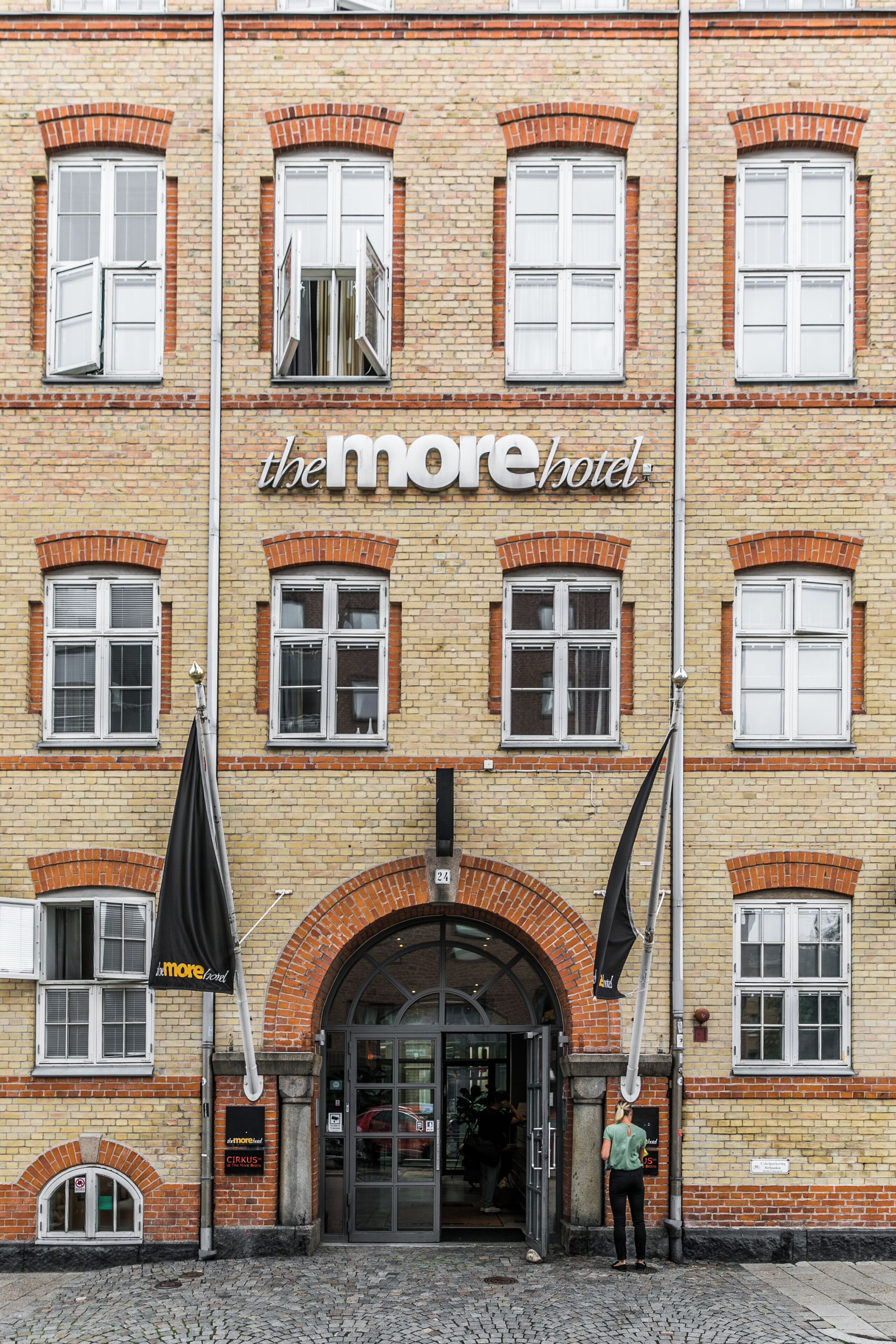 En byggnad med en skylt där det står ”the more hotel”, och ett svart paraply står framför ingången.