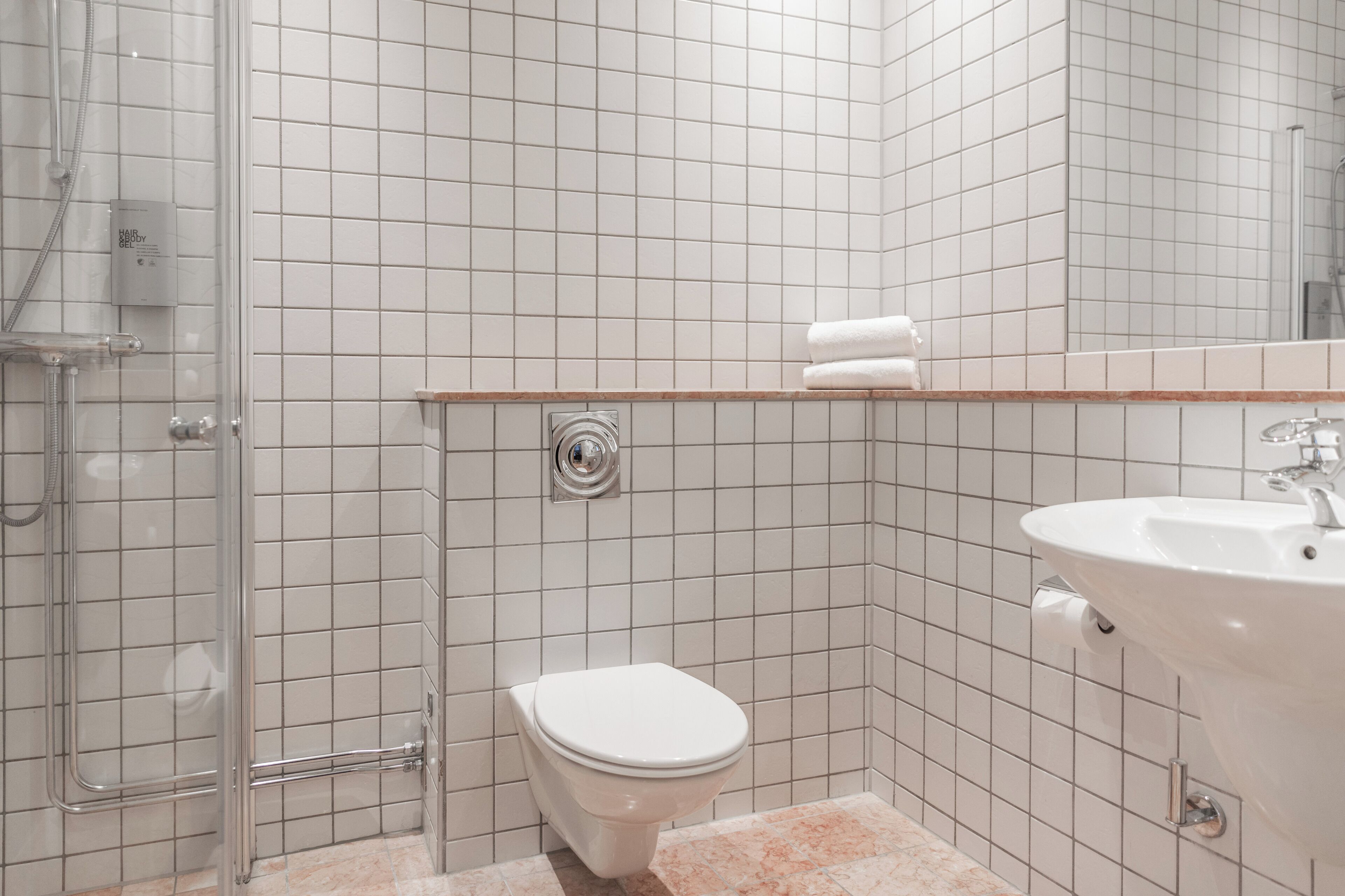 Een badkamer met een douchecabine van glas, een wit toilet en een wastafel met spiegel.