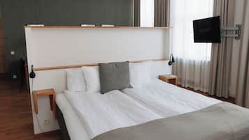 A modern hotel room with a large bed, bedside tables, a flat-screen TV, and a window with curtains.