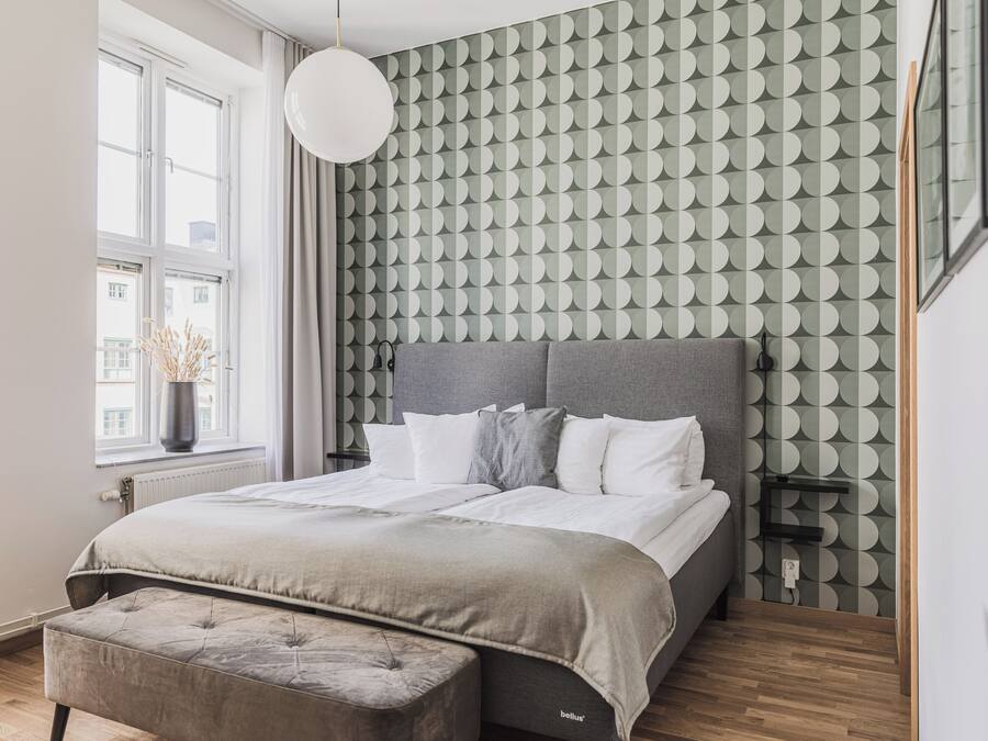 A modern bedroom with a grey upholstered bed, a grey headboard, and a patterned wallpaper.