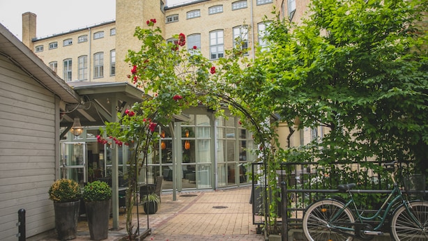 A brick-paved courtyard with a bicycle, potted plants, and a building entrance. - The More Hotel Mazetti (Malmö)