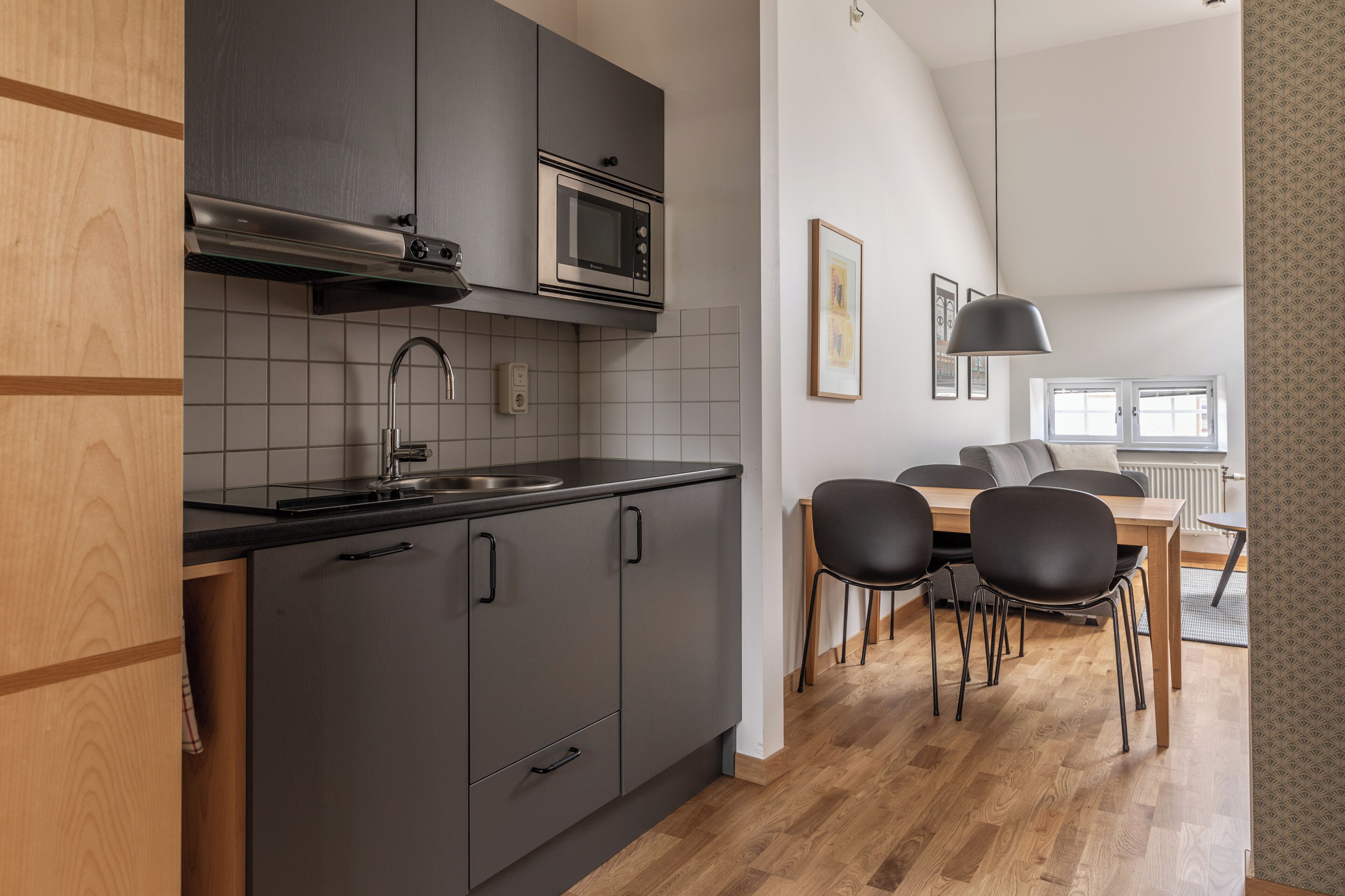 Una cucina moderna con mobili grigi, un lavello in acciaio inossidabile e un forno a microonde. C'è una zona pranzo con un tavolo in legno e sedie nere.
