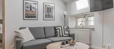 Uma sala de estar moderna com um sofá cinzento, uma mesa de centro redonda e duas fotos emolduradas na parede.