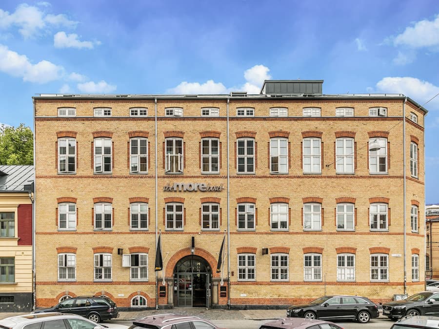 A multi-story brick building with a central entrance, multiple windows, and a sign that reads "the more hotel".