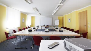 A conference room with a long table, red chairs, a whiteboard, and a projector. - Huberhof (Allershausen)
