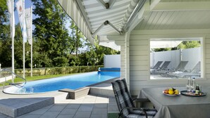 A covered outdoor area with a pool, lounge chairs, and a table with drinks and fruit. - Huberhof (Allershausen)