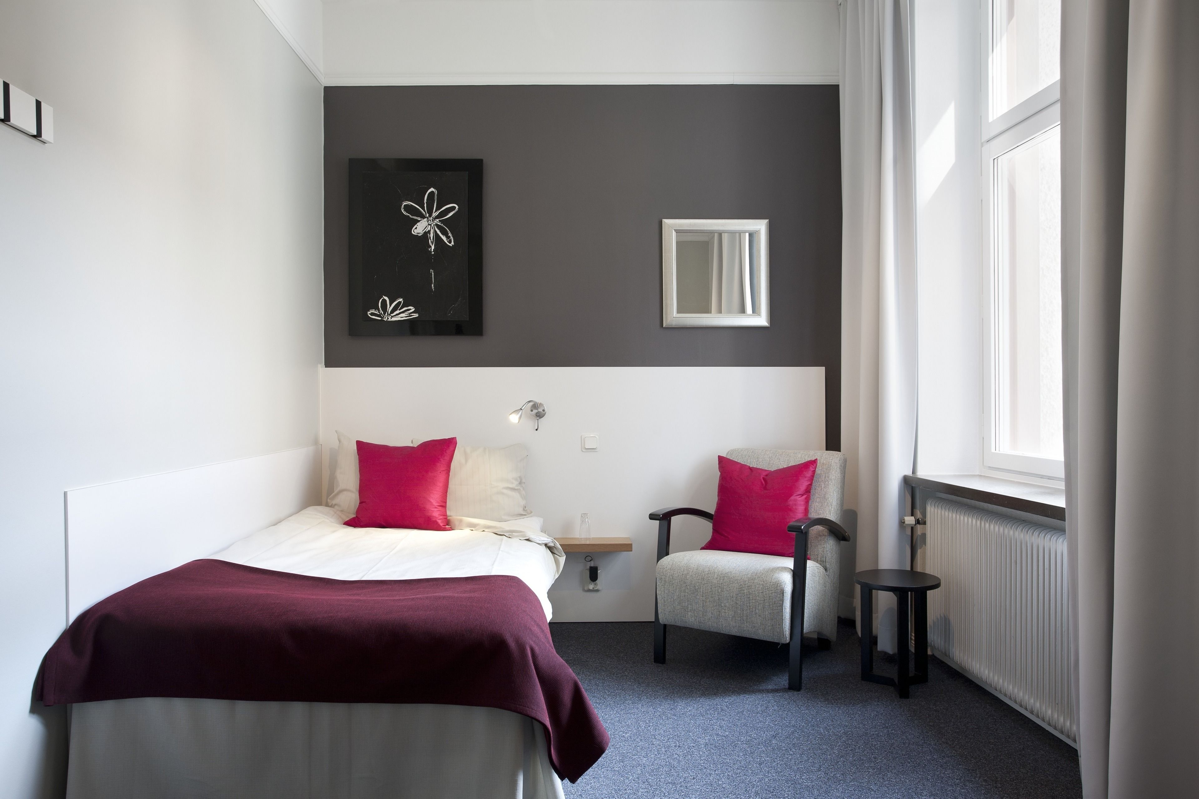 A hotel room with a bed, two chairs, a small table, a mirror, and artwork on the wall.