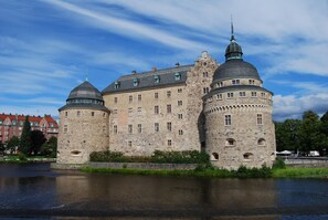 A historic stone castle with two prominent towers and a large central building, situated by a calm body of water.