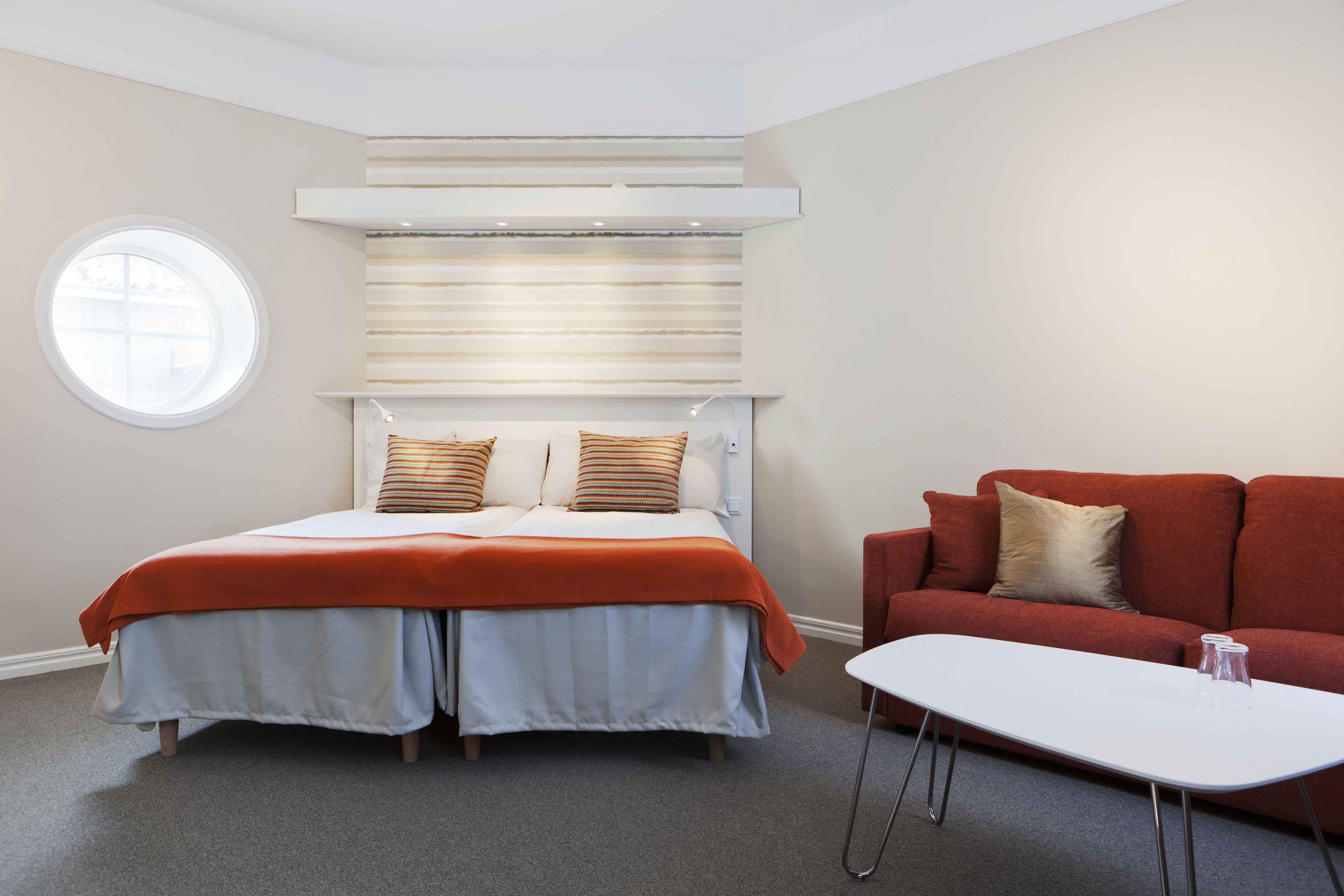 A bedroom with a bed, a red sofa, a white coffee table, and a window.