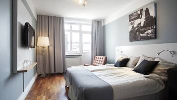 Habitación de hotel con cama, una silla, televisor, lámpara y ventana con cortinas.