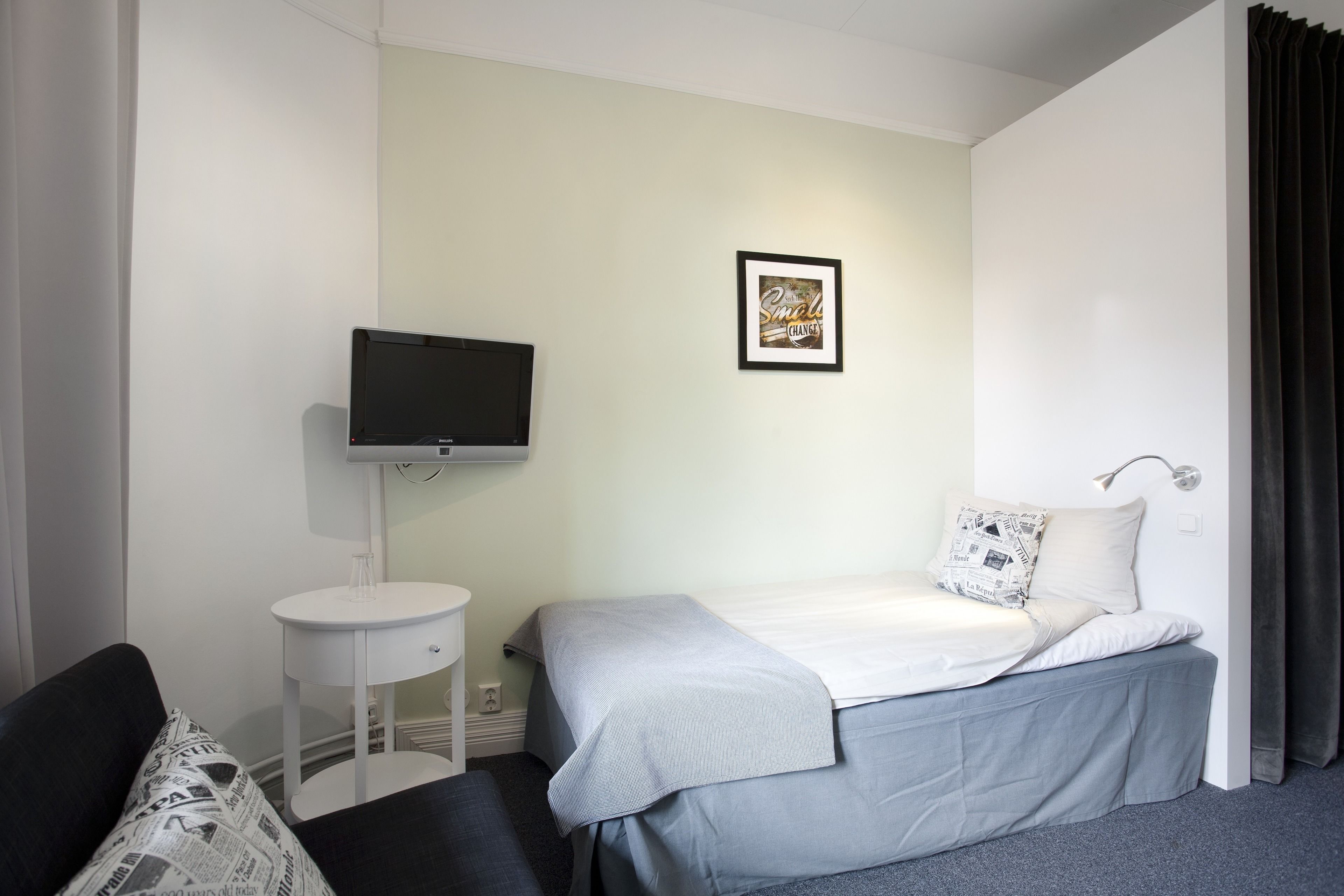 A hotel room with a bed, a TV, a small white table, and a framed picture on the wall.