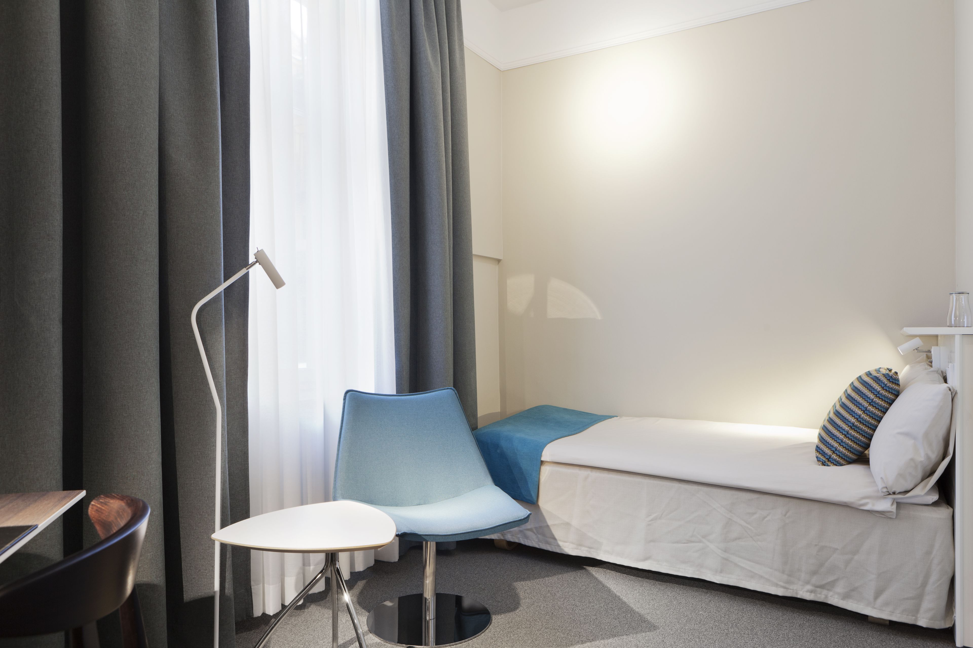 A hotel room with a single bed, a small table, a chair, and a desk.