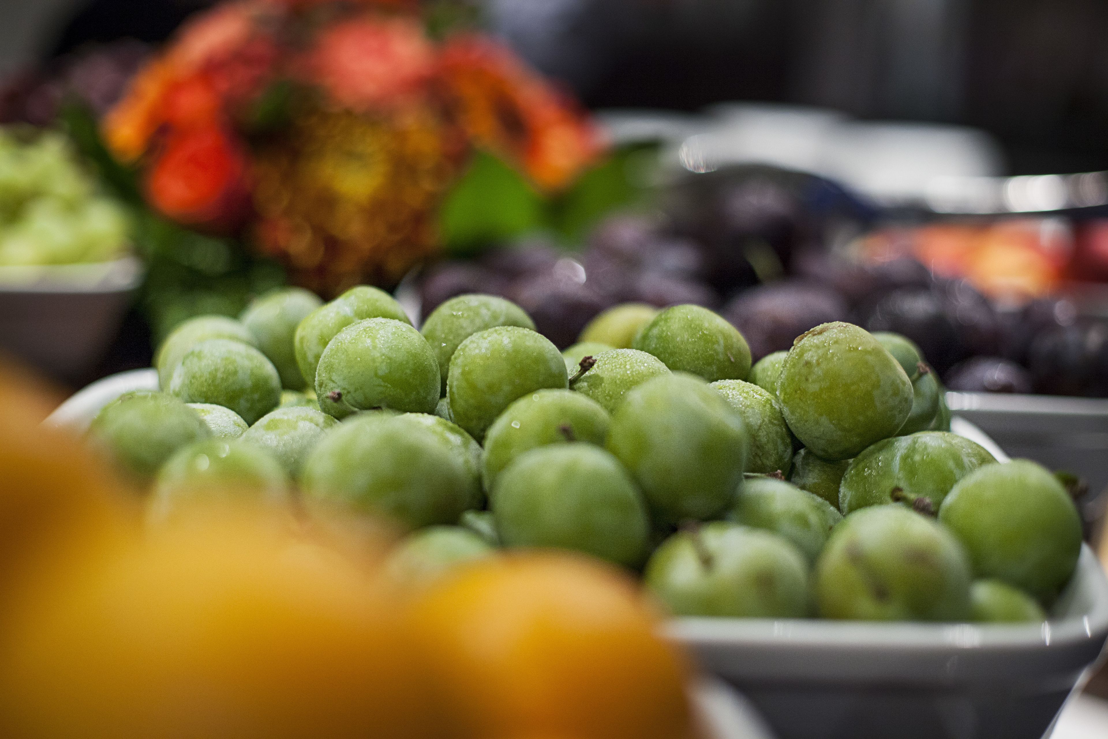 A bowl of green apples with a blurred background of other fruits.