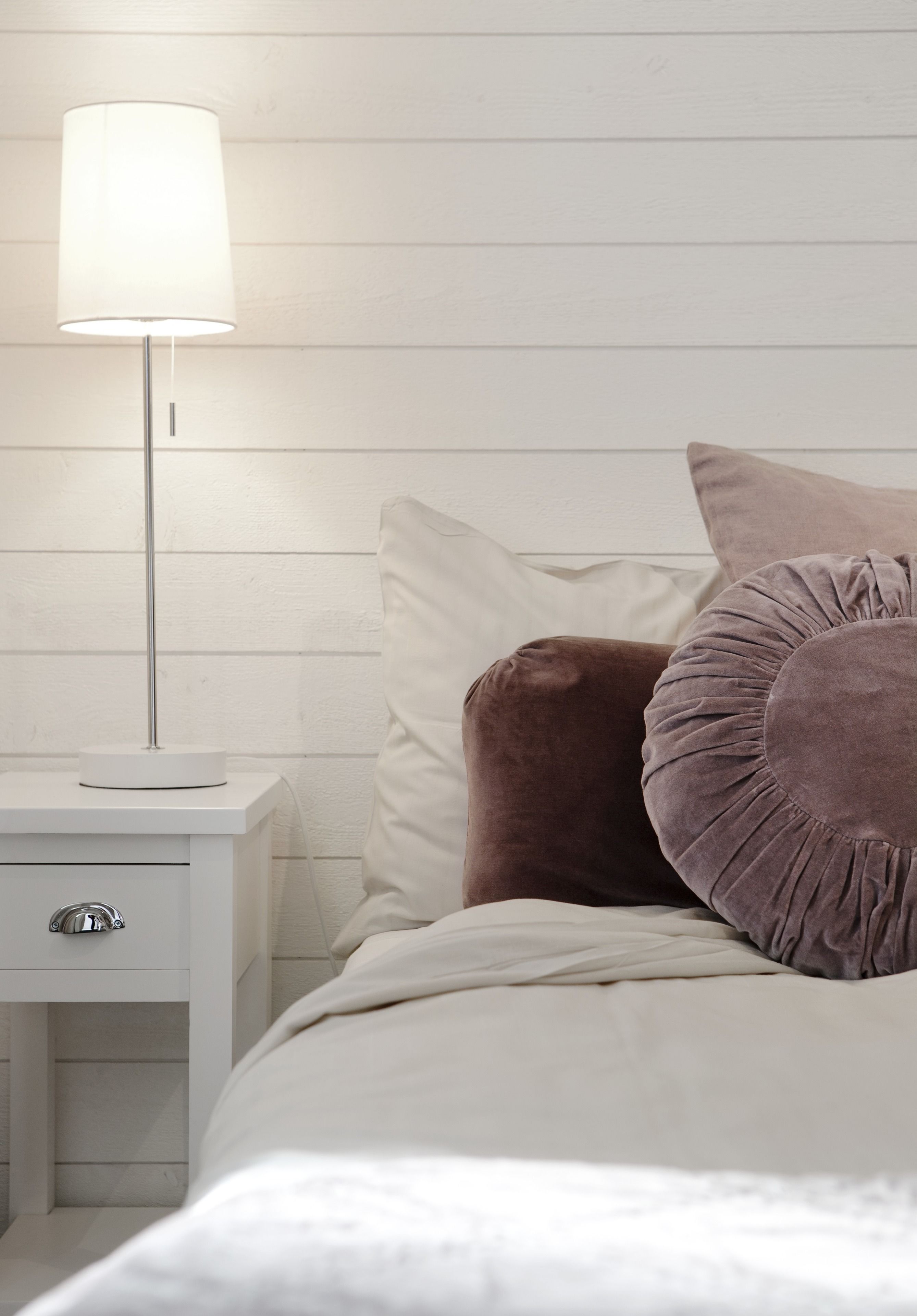 A neatly made bed with a white comforter and two pillows, one of which is brown.