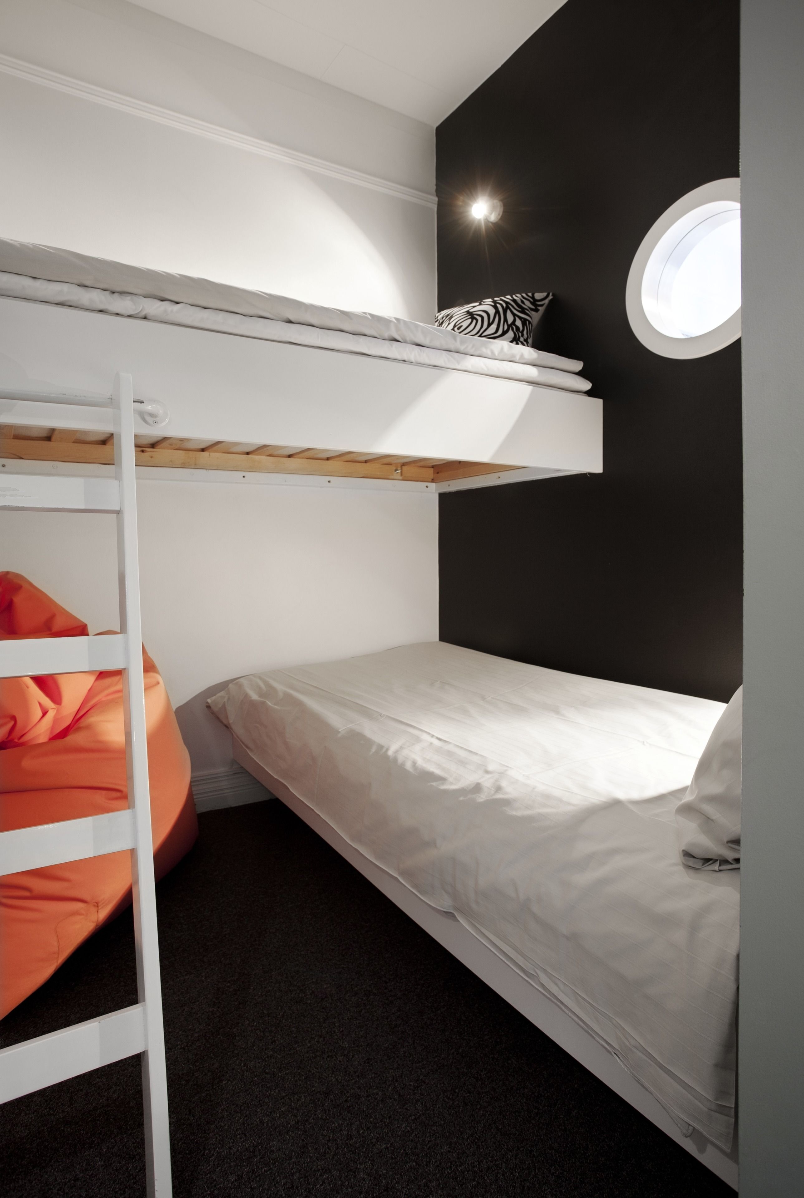 Un lit superposé avec une literie blanche et un pouf orange.