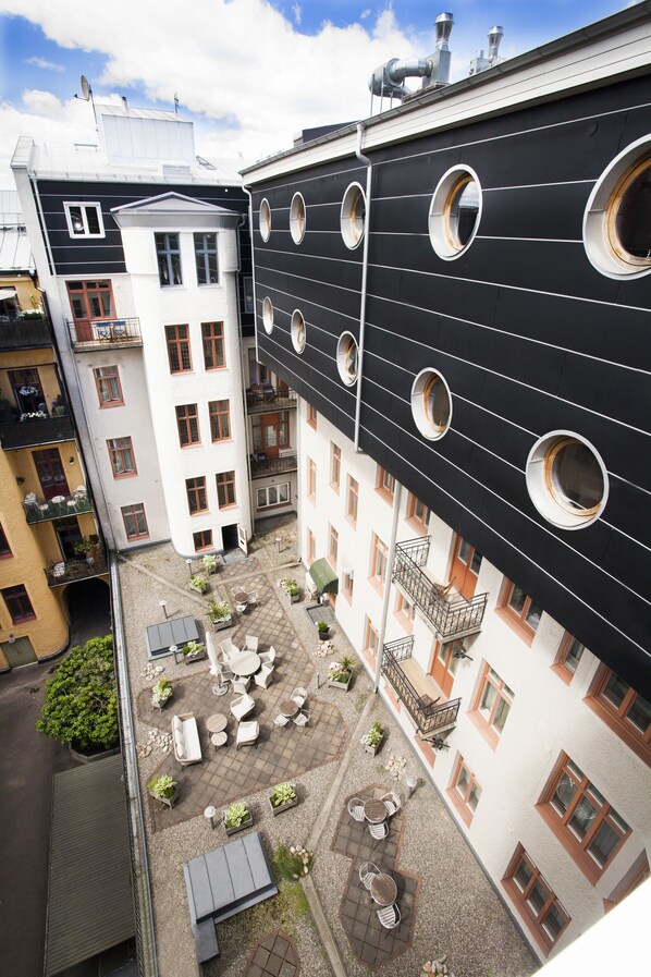 Um pátio com mesas ao ar livre, um edifício com janelas circulares e um terraço com antenas parabólicas.