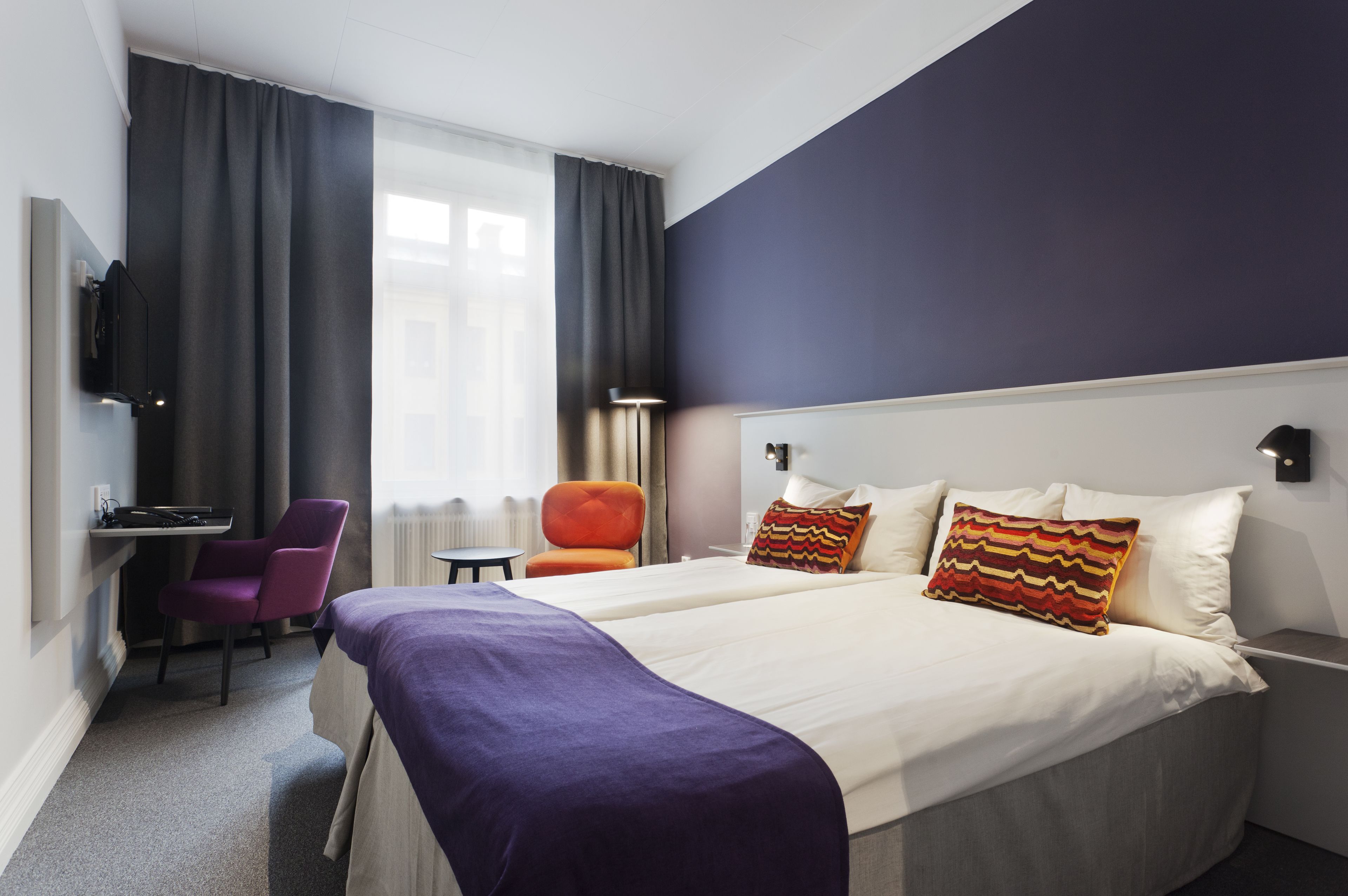 Une chambre d’hôtel avec un grand lit, deux oreillers, un bureau avec une chaise et une fenêtre avec des rideaux.
