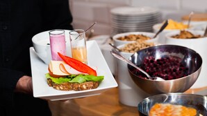 A buffet table with various food items including a sandwich, bowls of fruit, and a bowl of granola.