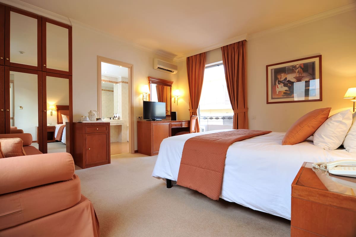 A hotel room with a large bed, a desk with a computer, a TV, and a bathroom visible through an open door.