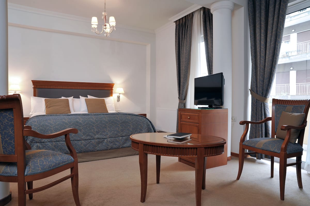 A hotel room with a bed, two wooden chairs, a small round table, a TV, and a view of the outside balcony.