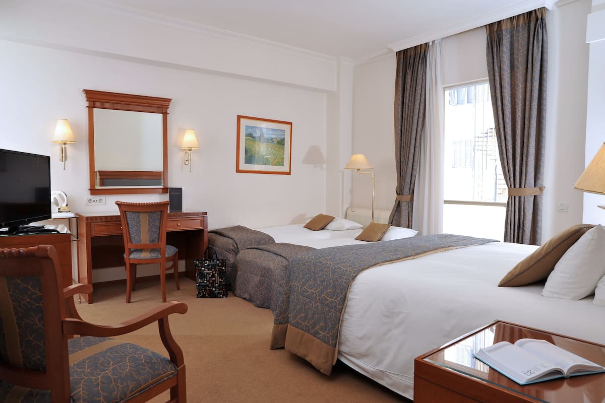 A hotel room with a desk, two beds, a chair, a television, and a window with curtains.