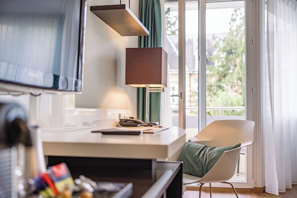 Habitación moderna con escritorio, silla, lámpara y vistas a través de un ventanal.