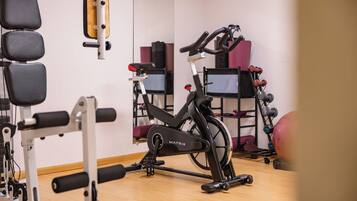 Uma academia com equipamentos de ginástica, incluindo uma bicicleta ergométrica, pesos e um banco.