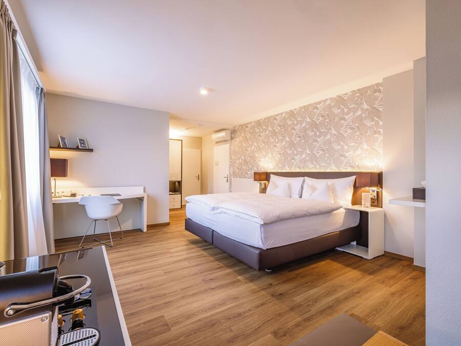 A modern hotel room with a bed, bedside table, and a desk with a chair.