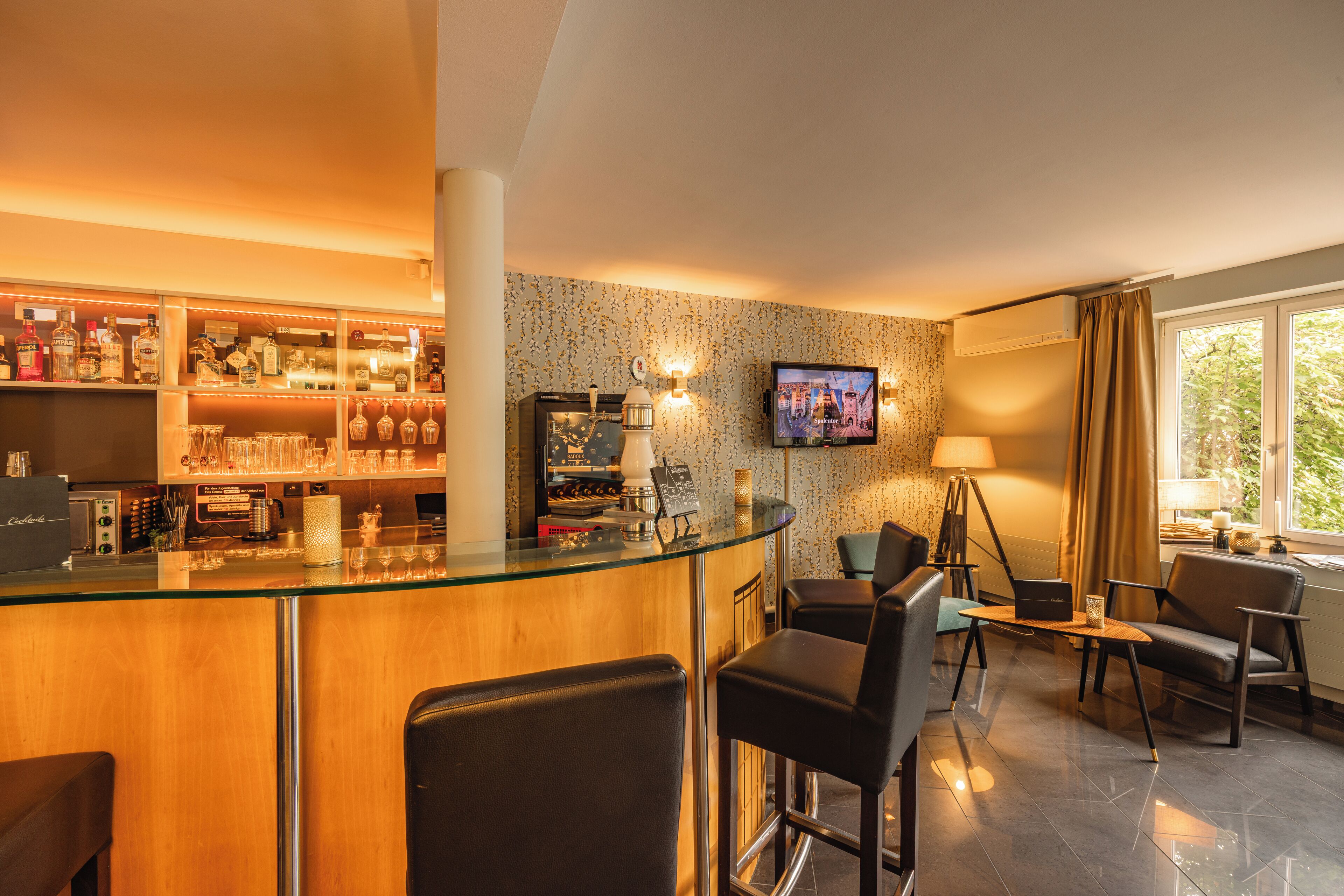 A bar area with a glass counter, bar stools, and a television mounted on the wall.