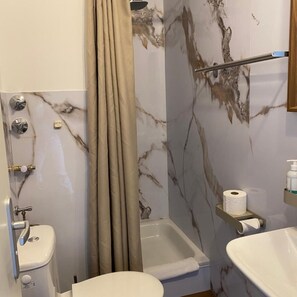 A bathroom with a shower, toilet, and sink, marble walls, and a towel rack. - City-Hotel Frankfurt (Frankfurt)