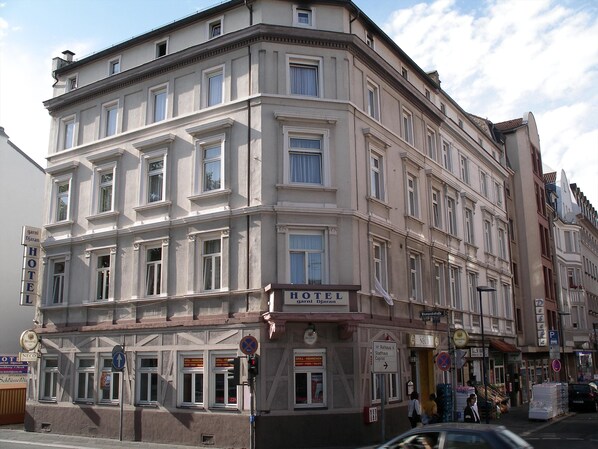 Un hôtel à plusieurs étages, de style architectural classique, qui se distingue par une grande enseigne « HÔTEL » placée au niveau du rez-de-chaussée.