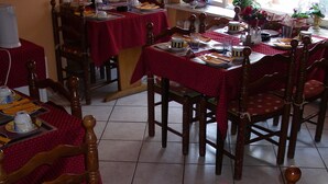 Een eetruimte met meerdere tafels gedekt voor maaltijden, met rode tafelkleden en houten stoelen.