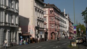 Straatbeeld met een hotel genaamd "HOTEL garni" aan de linkerkant, met klassieke architectuur, grote ramen en een balkon.