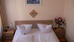 Een hotelkamer met een groot bed, twee kussens, een nachtkastje met een lamp, een vaas met bloemen en een lijst met een afbeelding aan de muur.