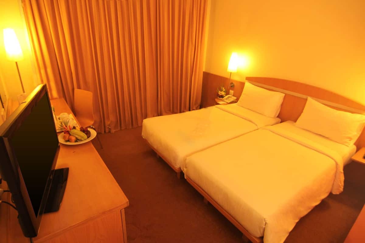A hotel room with a bed, a desk with a computer, and a lamp.