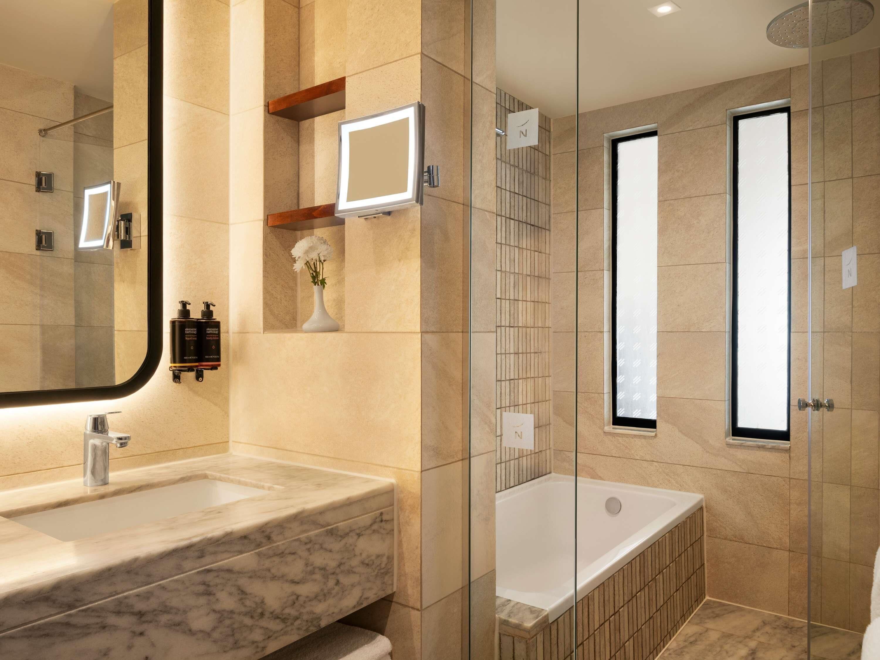 Un baño moderno con lavamanos de mármol, un espejo grande, zona de ducha y bañera.
