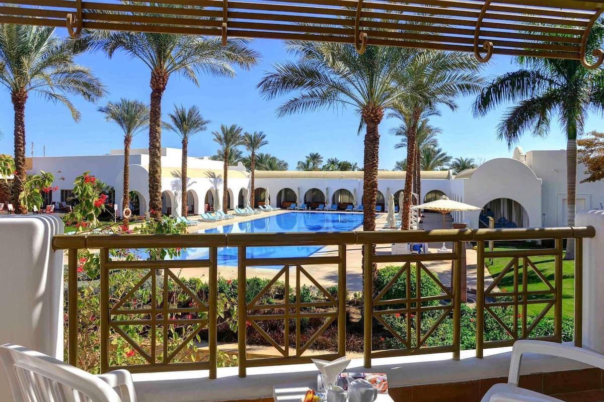 A poolside area with a view of a pool, palm trees, and a building with arches.
