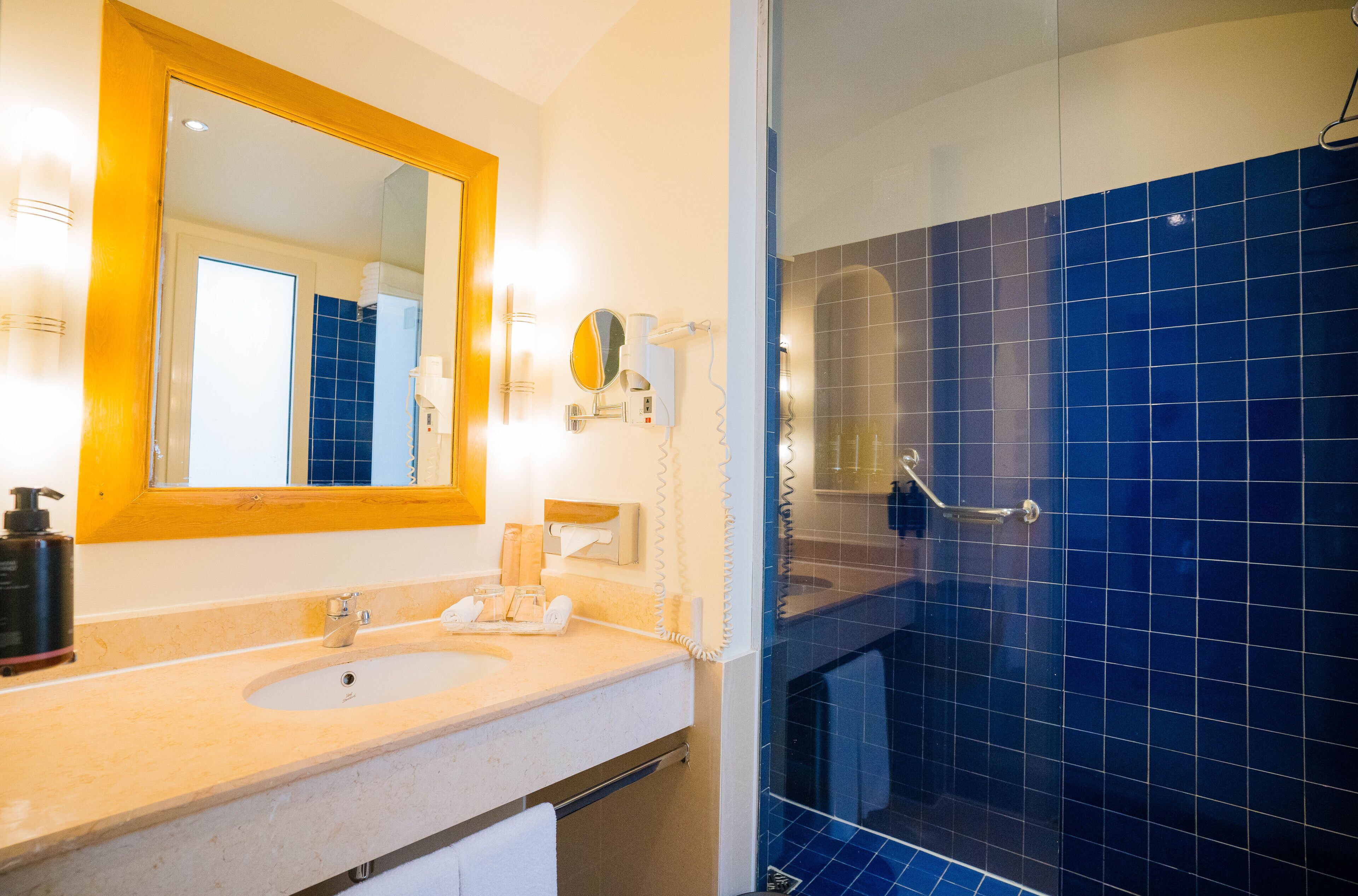 Un baño con lavamanos, espejo y zona de ducha con azulejos azules.
