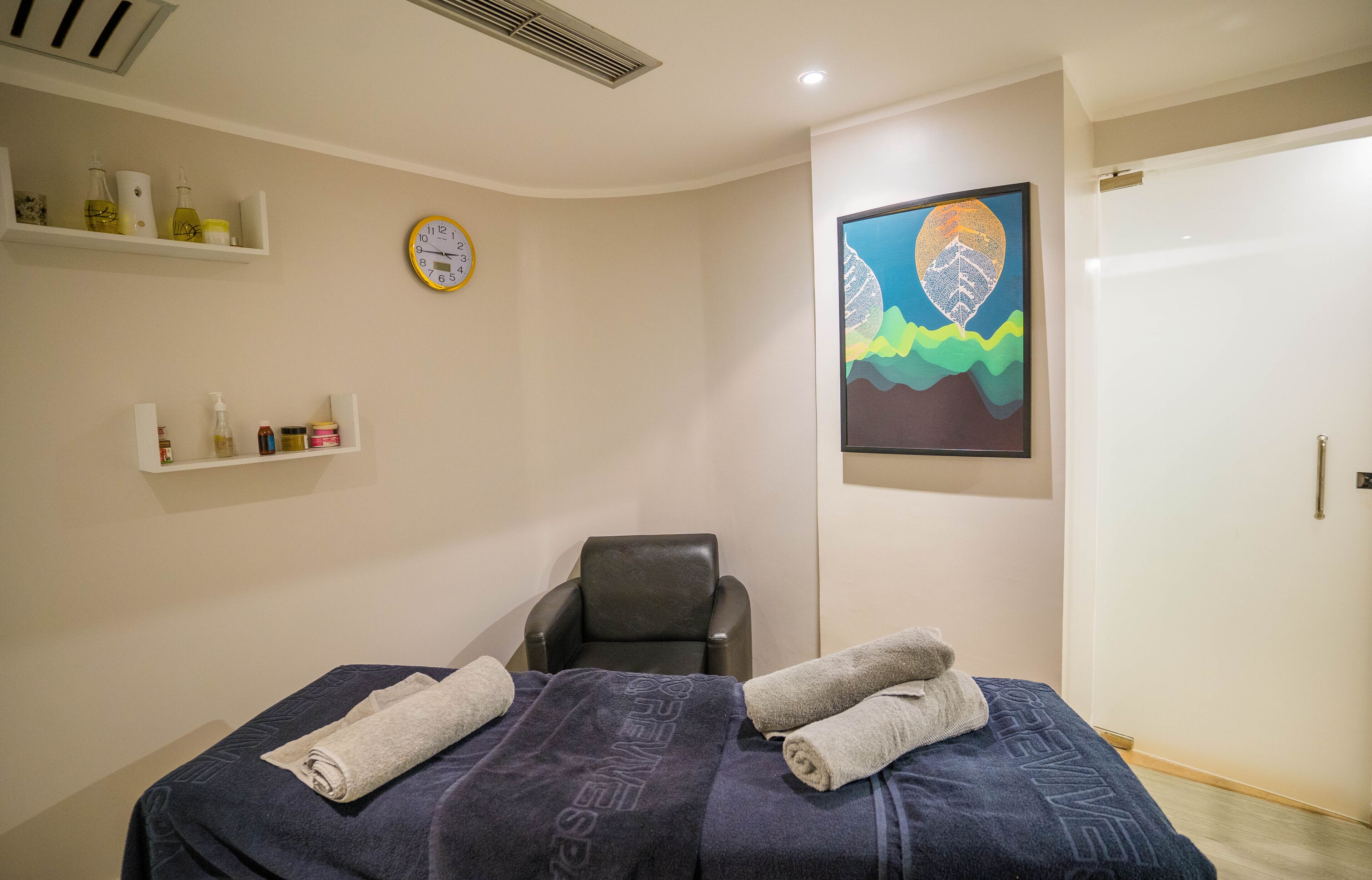 Una habitación con cama, una silla, un reloj y estantes con artículos de aseo.