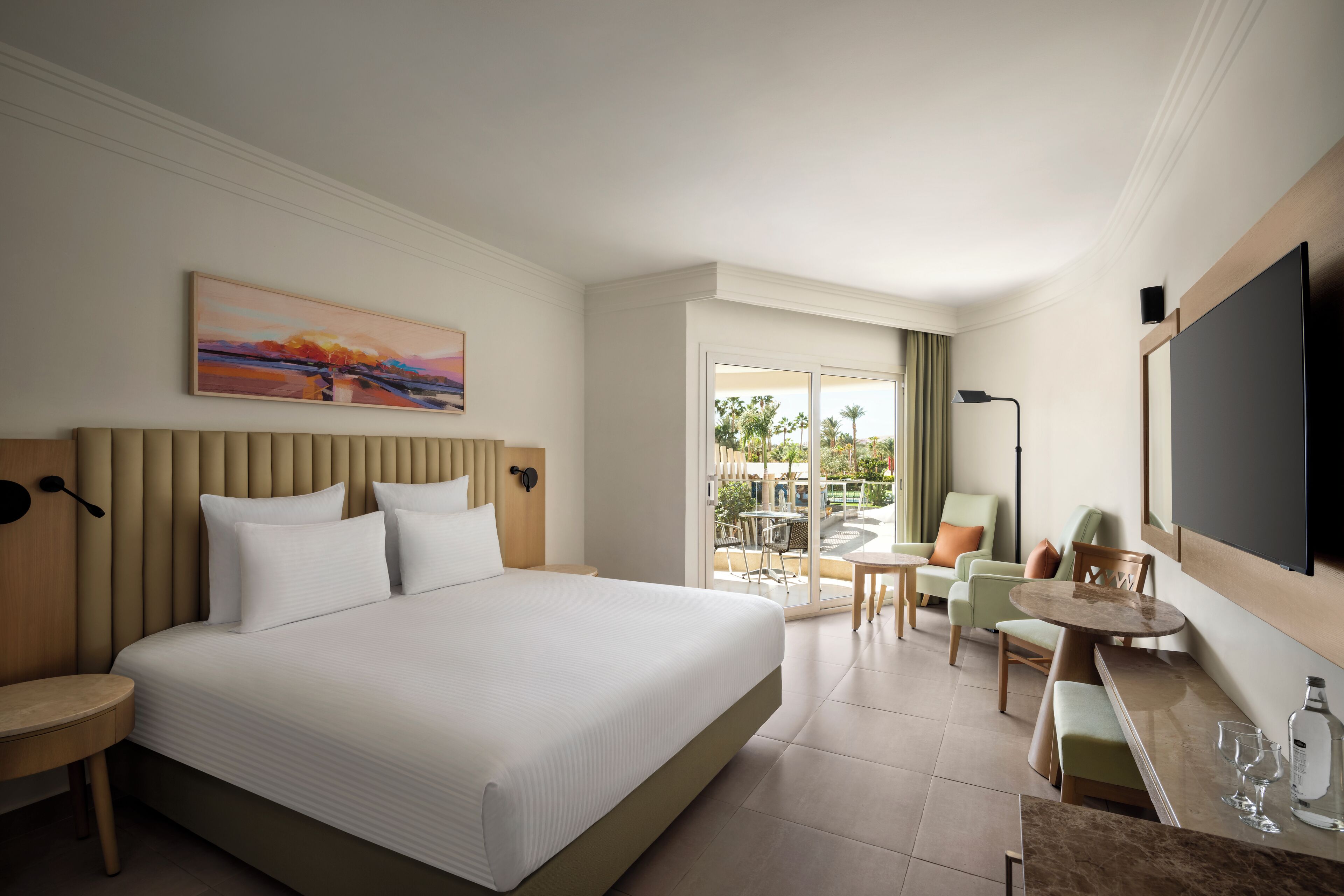 A hotel room with a large bed, a desk, a chair, and a TV.