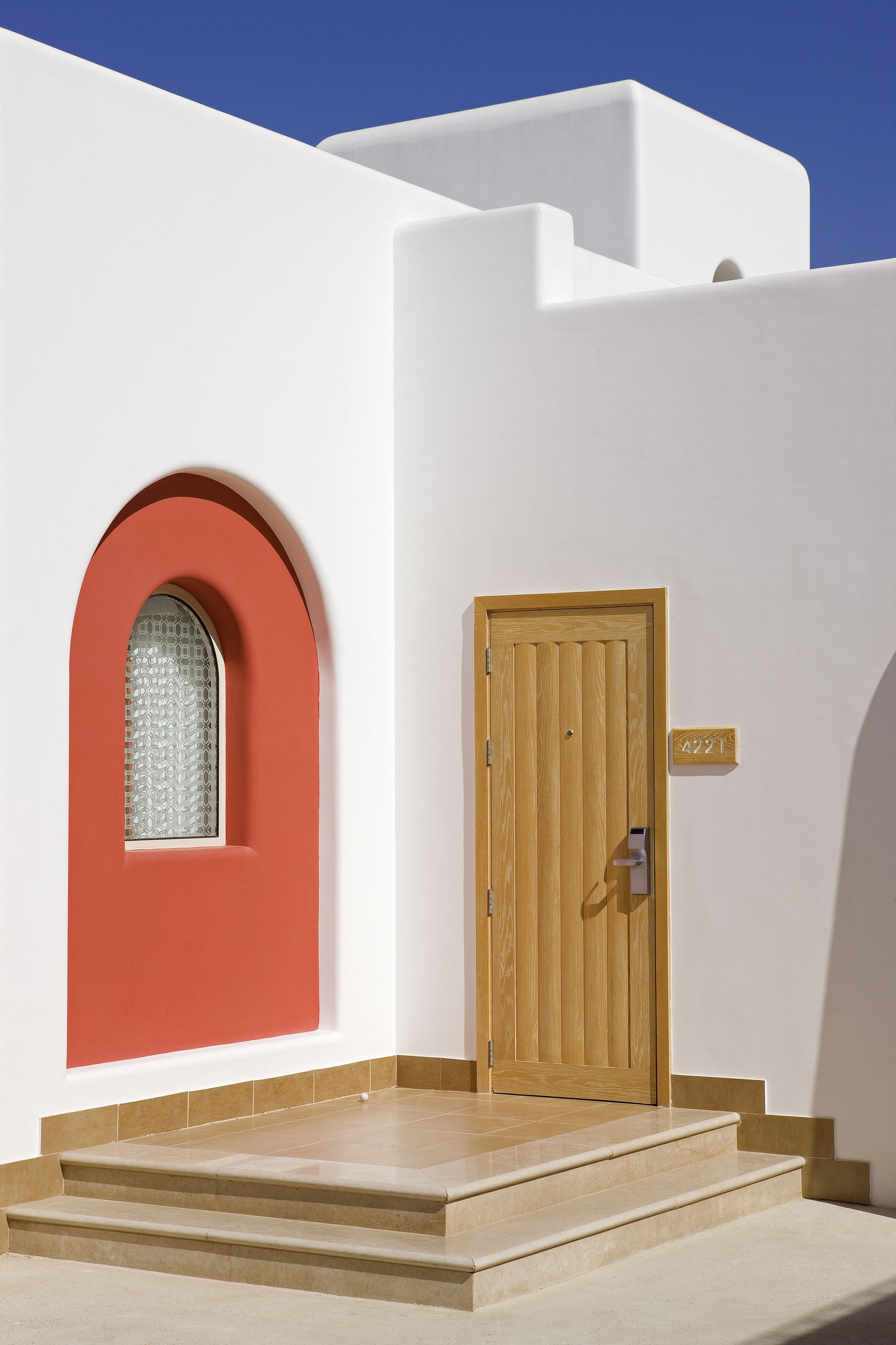 A white building with a red arched window and a wooden door with a number plaque.