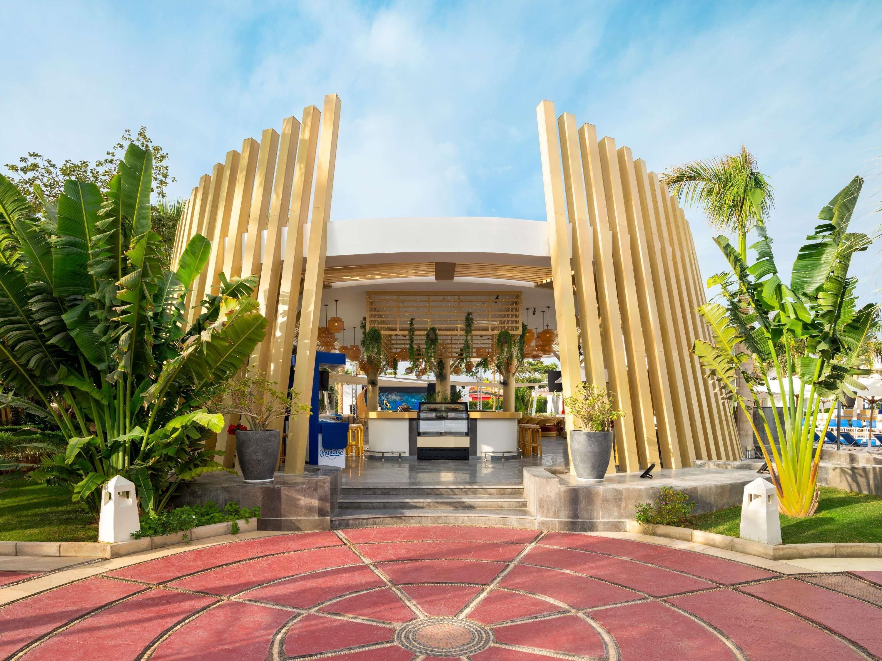 Entrada de hotel con suelo de estampado rojo, un mostrador de recepción central y paneles de madera verticales.