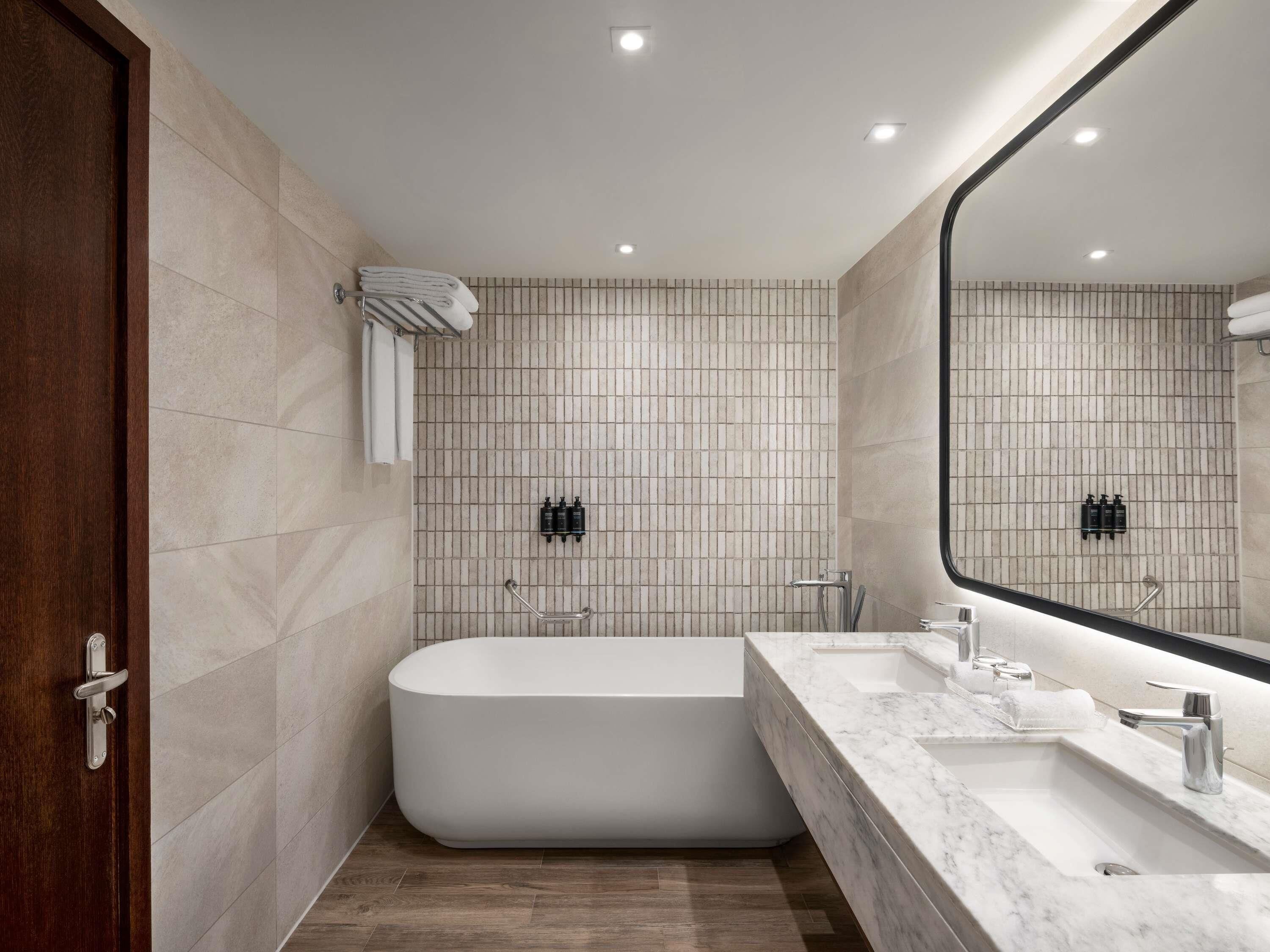 Un baño moderno con una bañera independiente, un espejo grande y una encimera de mármol.